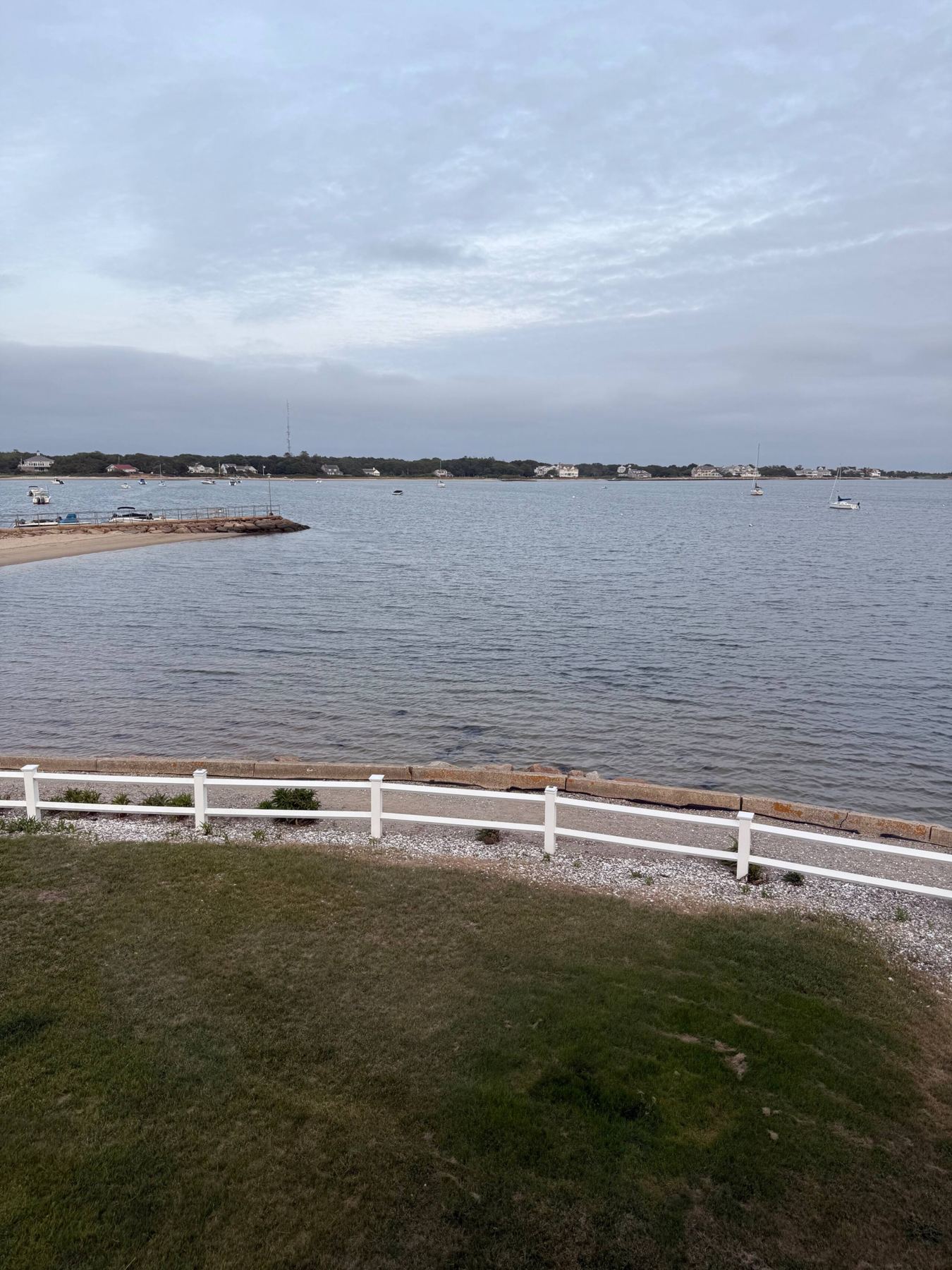 View across the lawn and white fence to the bay with moored sailboats