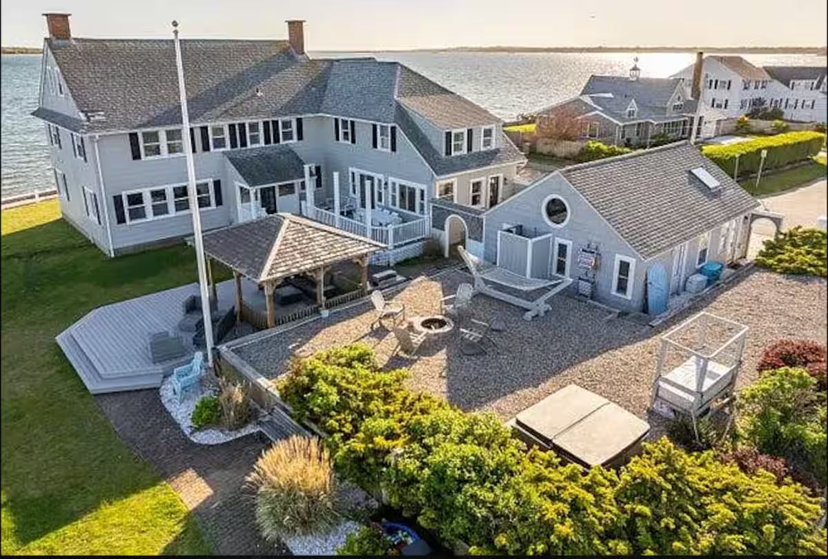 The house and guest cottage from above, with the bay behind, a fire pit and a covered deck